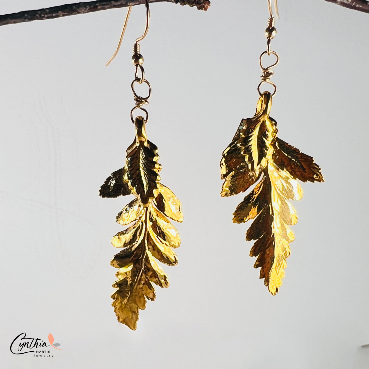 Shiny fern-shaped gold dangle earrings twinkle as they weave through hair, reflecting the essence of Mother Nature.