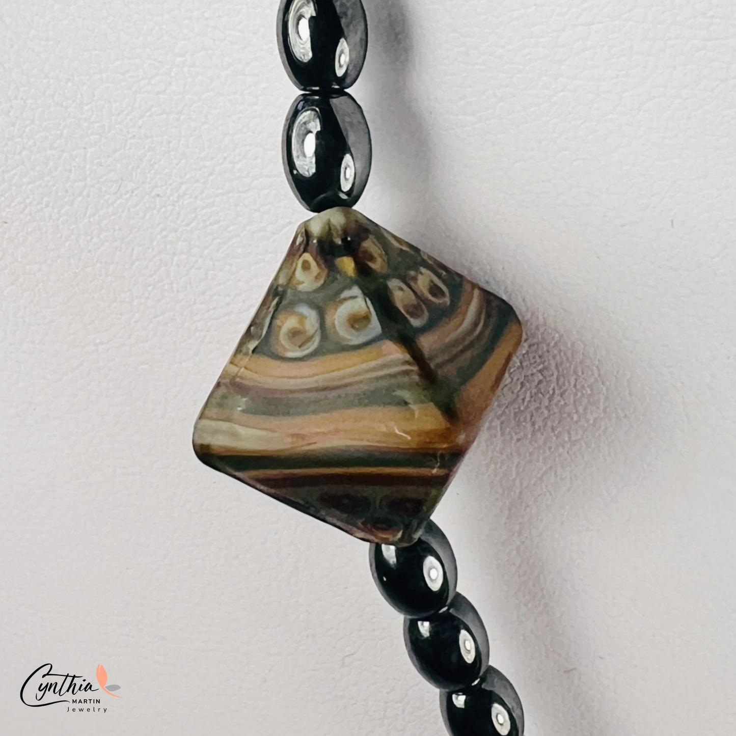 Necklace featuring an ancient two-eye Dzi bead from Nepal, paired with handcrafted pyramid-shaped ceramic beads and egg-shaped hematite beads, 15 inches with a 2-inch extender.