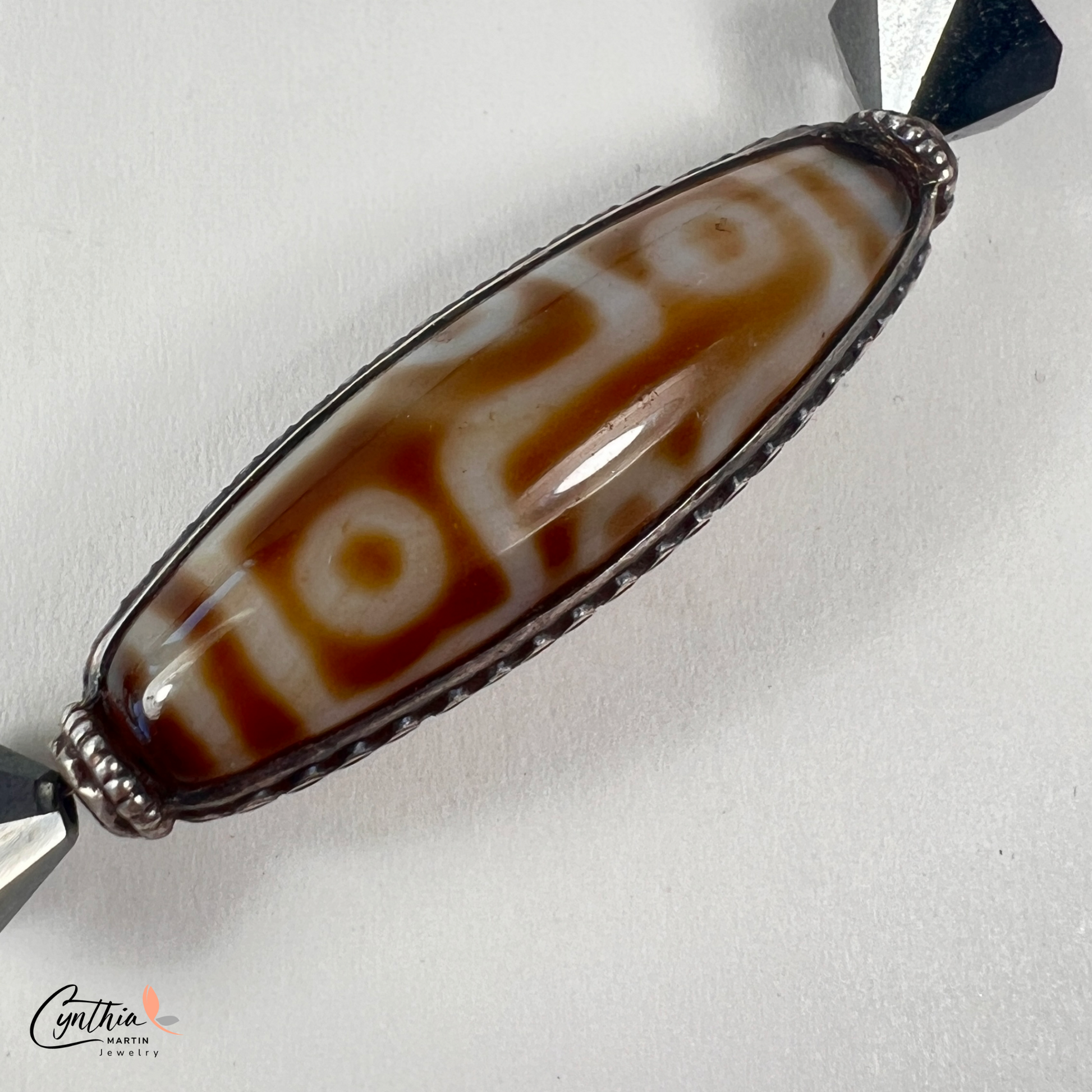 Necklace featuring an ancient two-eye Dzi bead from Nepal, paired with handcrafted pyramid-shaped ceramic beads and egg-shaped hematite beads, 15 inches with a 2-inch extender.