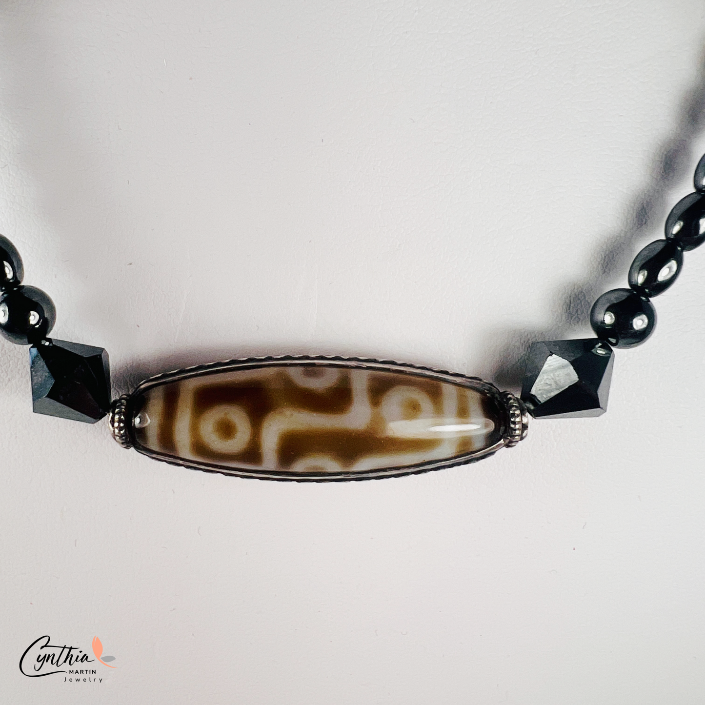 Necklace featuring an ancient two-eye Dzi bead from Nepal, paired with handcrafted pyramid-shaped ceramic beads and egg-shaped hematite beads, 15 inches with a 2-inch extender.