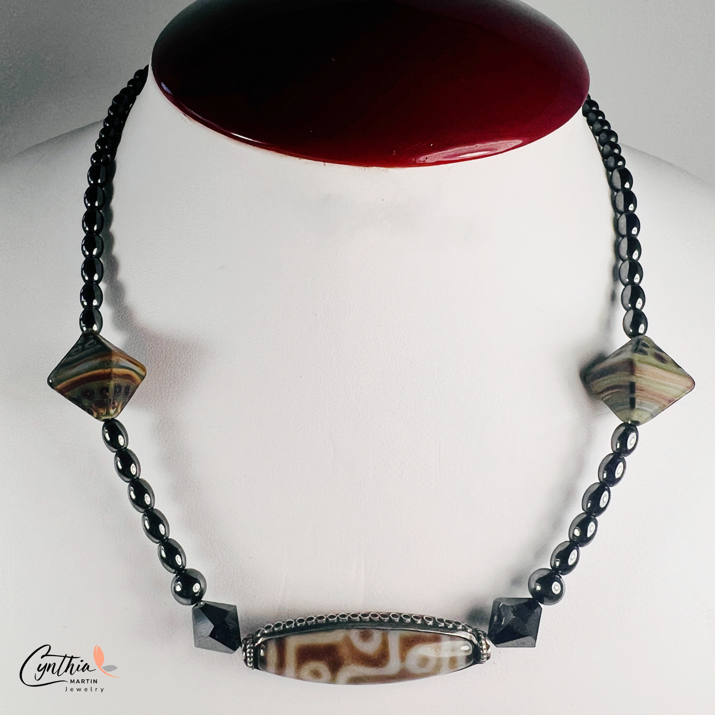 Necklace featuring an ancient two-eye Dzi bead from Nepal, paired with handcrafted pyramid-shaped ceramic beads and egg-shaped hematite beads, 15 inches with a 2-inch extender.