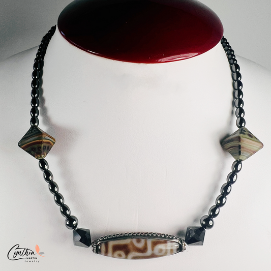Necklace featuring an ancient two-eye Dzi bead from Nepal, paired with handcrafted pyramid-shaped ceramic beads and egg-shaped hematite beads, 15 inches with a 2-inch extender.