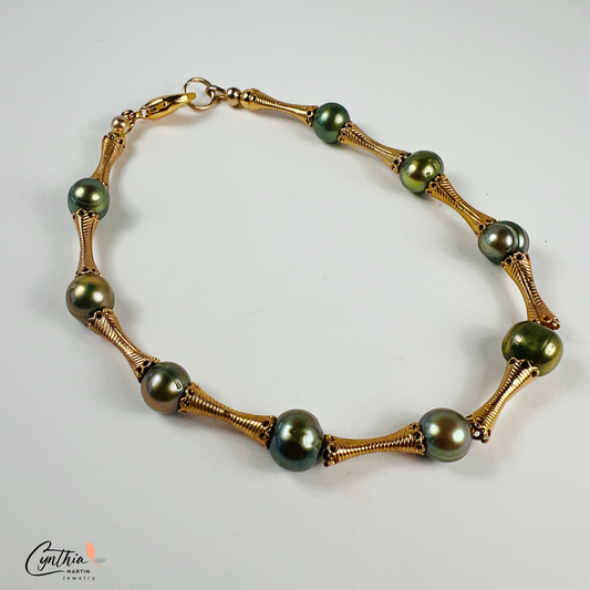 Stylish bracelet with iridescent green pearls and gold tube spacers, perfect for casual or corporate attire.