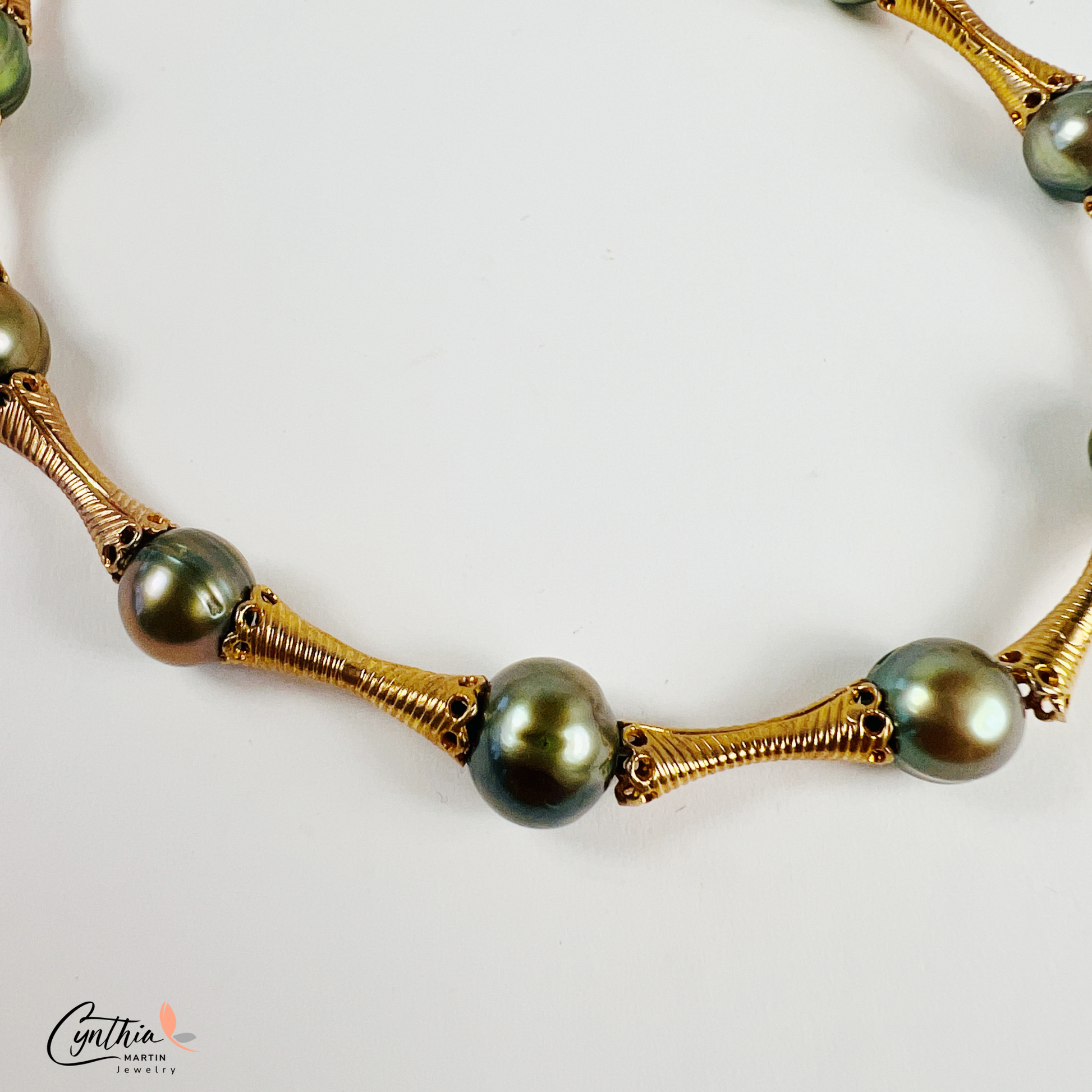Stylish bracelet with iridescent green pearls and gold tube spacers, perfect for casual or corporate attire.