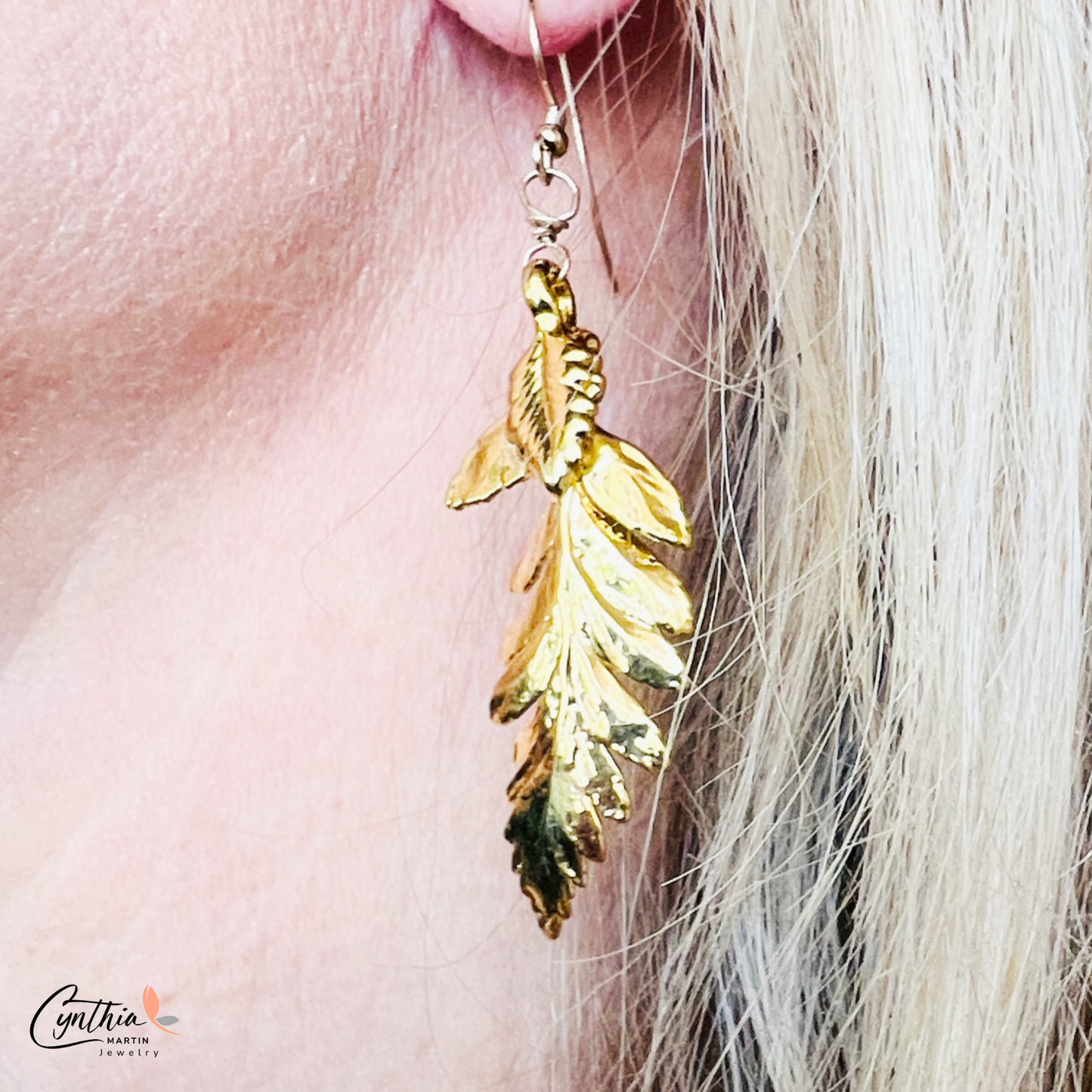 Shiny fern-shaped gold dangle earrings twinkle as they weave through hair, reflecting the essence of Mother Nature.