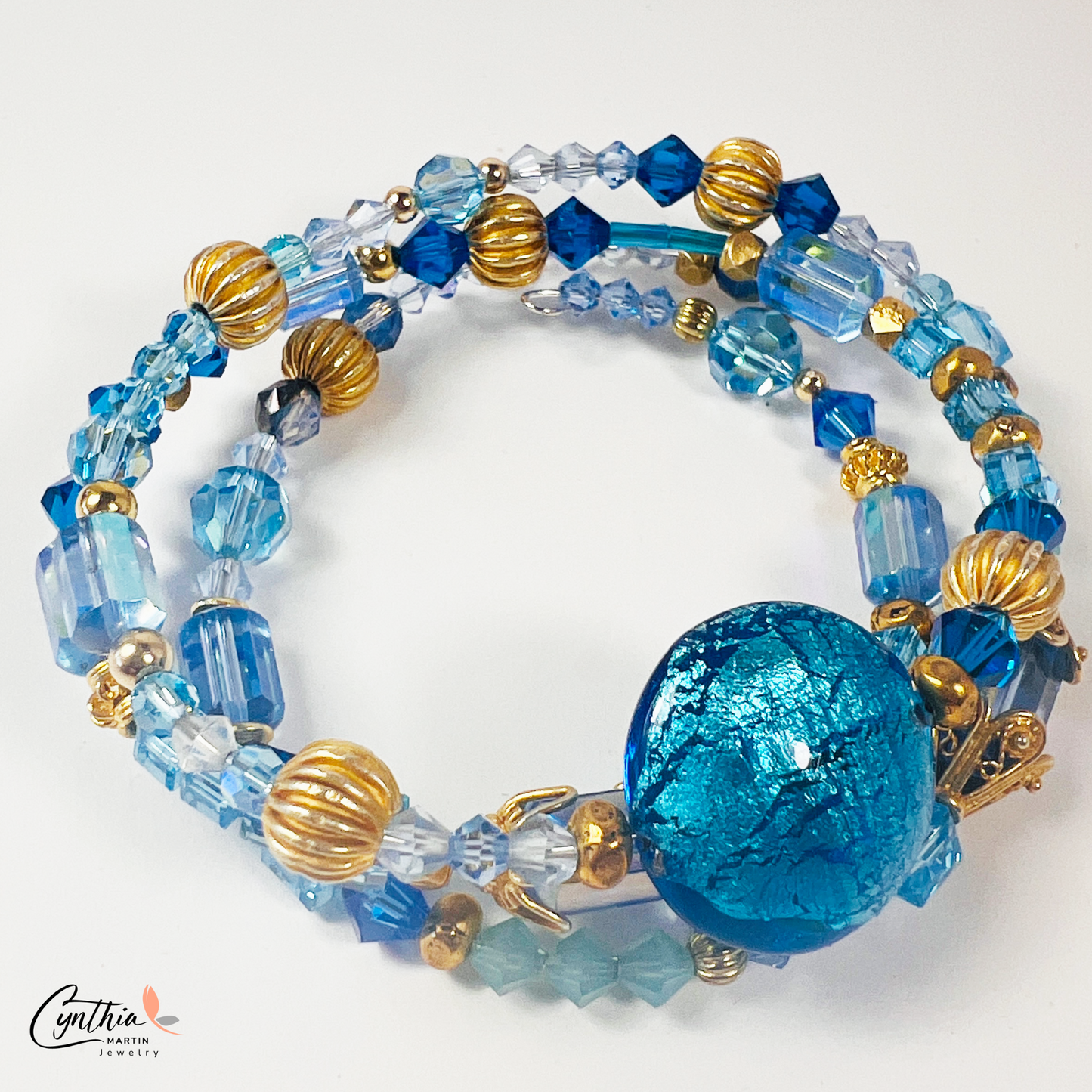 Three-wrap bracelet featuring a blue Italian Murano glass foiled focal bead, gold bead caps, transparent tube beads, and Swarovski crystals.