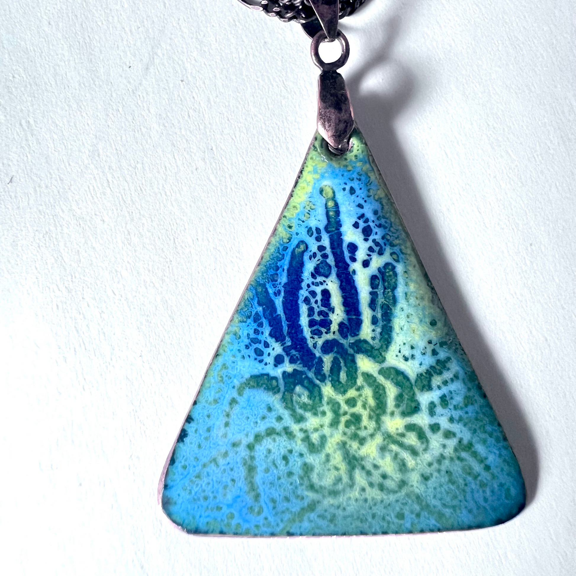 Striking pendant featuring an underwater scene crafted with six layers of multi-colored enamel using the sgraffito technique, showcasing vibrant marine life and aquatic elements, suspended from a dynamic tri-link copper chain.