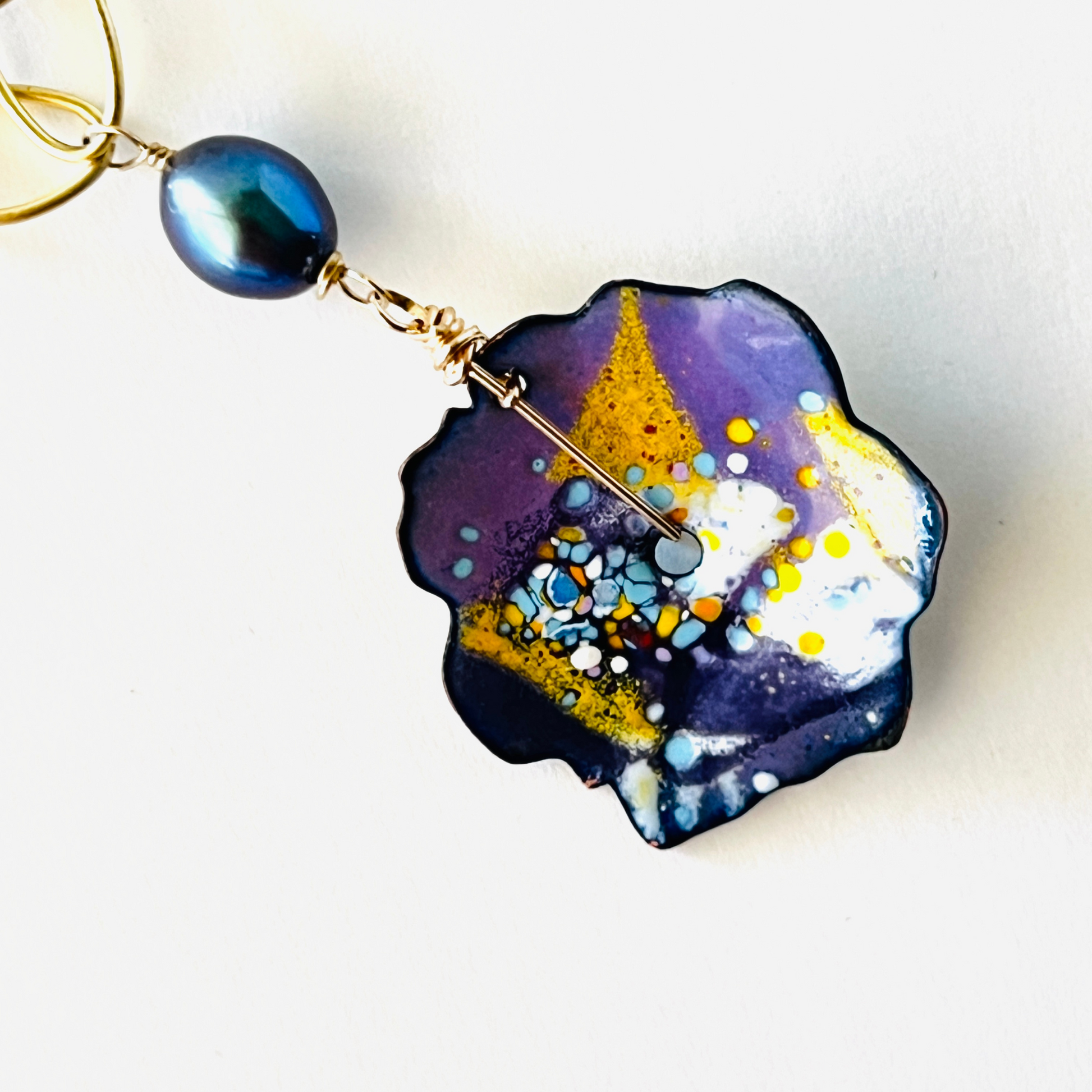 Enamel pendant with splashes of purple, orange, and yellow, hanging with a black pearl on a gold vermeil large link chain.