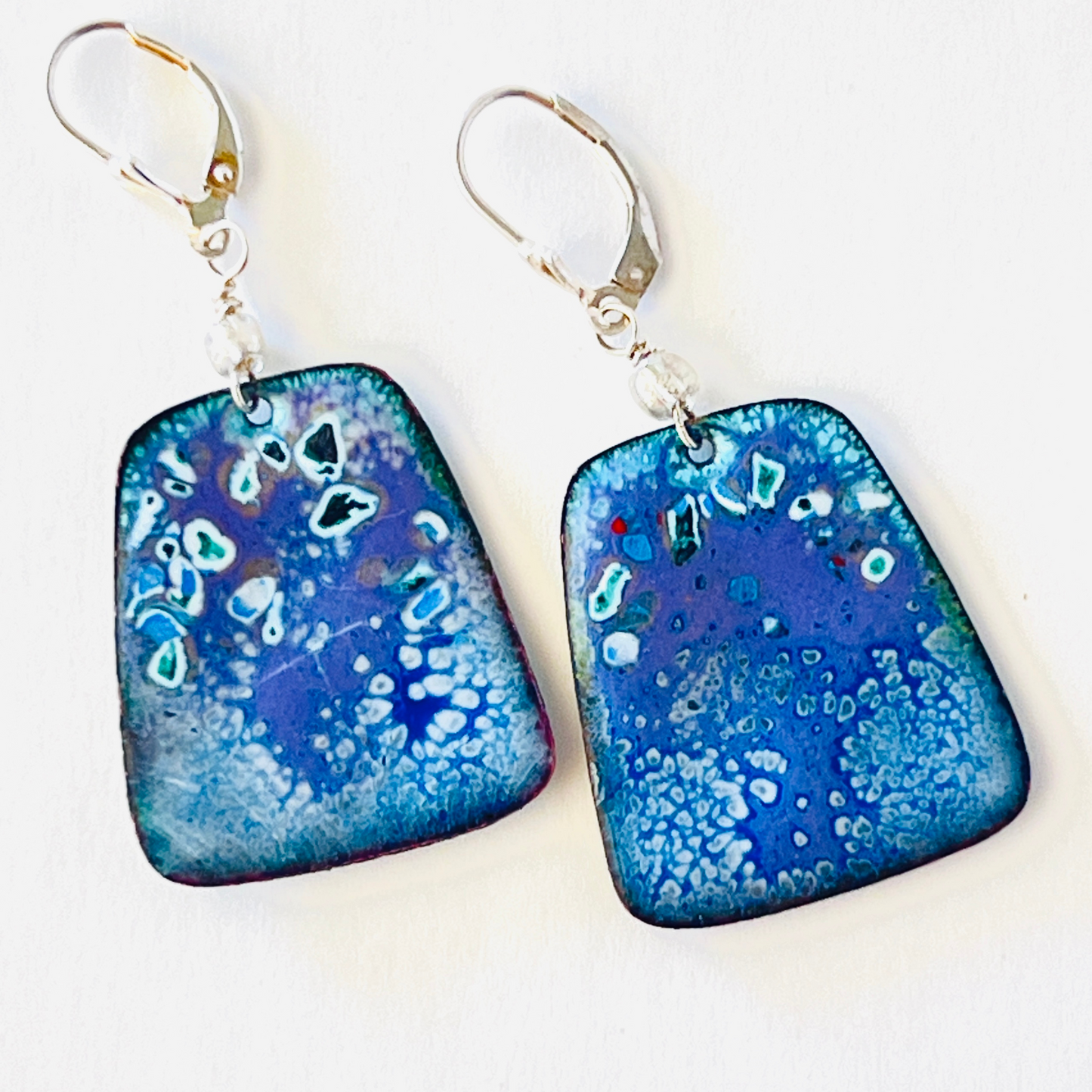 Torch-fired enamel earrings inspired by a blue sky over Tucson snow, hanging on sterling silver ear wires.