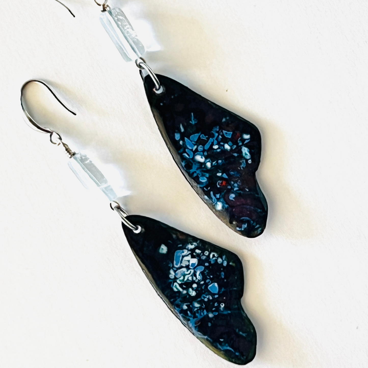 Torch-fired enamel earrings inspired by Tucson snow on a blue sky, hanging from sterling silver ear wires.