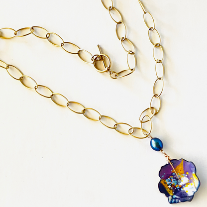 Enamel pendant with splashes of purple, orange, and yellow, hanging with a black pearl on a gold vermeil large link chain.