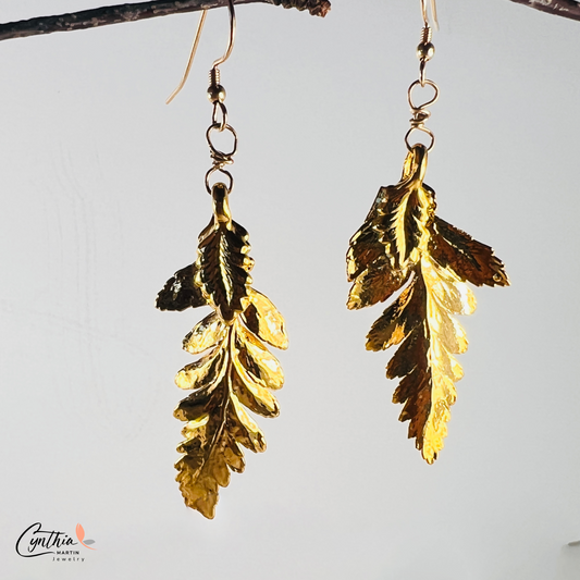 Shiny fern-shaped gold dangle earrings twinkle as they weave through hair, reflecting the essence of Mother Nature.
