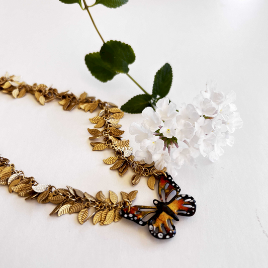 Kiln-fired monarch pendant nestled in intricate gold leaves on a necklace, hand-painted with liquid enamel watercolor.