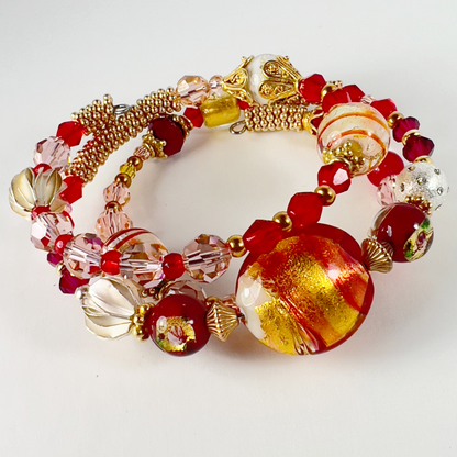 Delicate 3-wrap bracelet featuring a gold Italian Murano glass focal bead with swirls of orange, cream, red, and gold bead caps. Accented with sterling silver and gold-filled metals, handmade Hill Tribe sterling silver beads, and Swarovski crystals in pinks and reds.