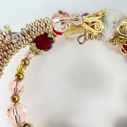 Delicate 3-wrap bracelet featuring a gold Italian Murano glass focal bead with swirls of orange, cream, red, and gold bead caps. Accented with sterling silver and gold-filled metals, handmade Hill Tribe sterling silver beads, and Swarovski crystals in pinks and reds.