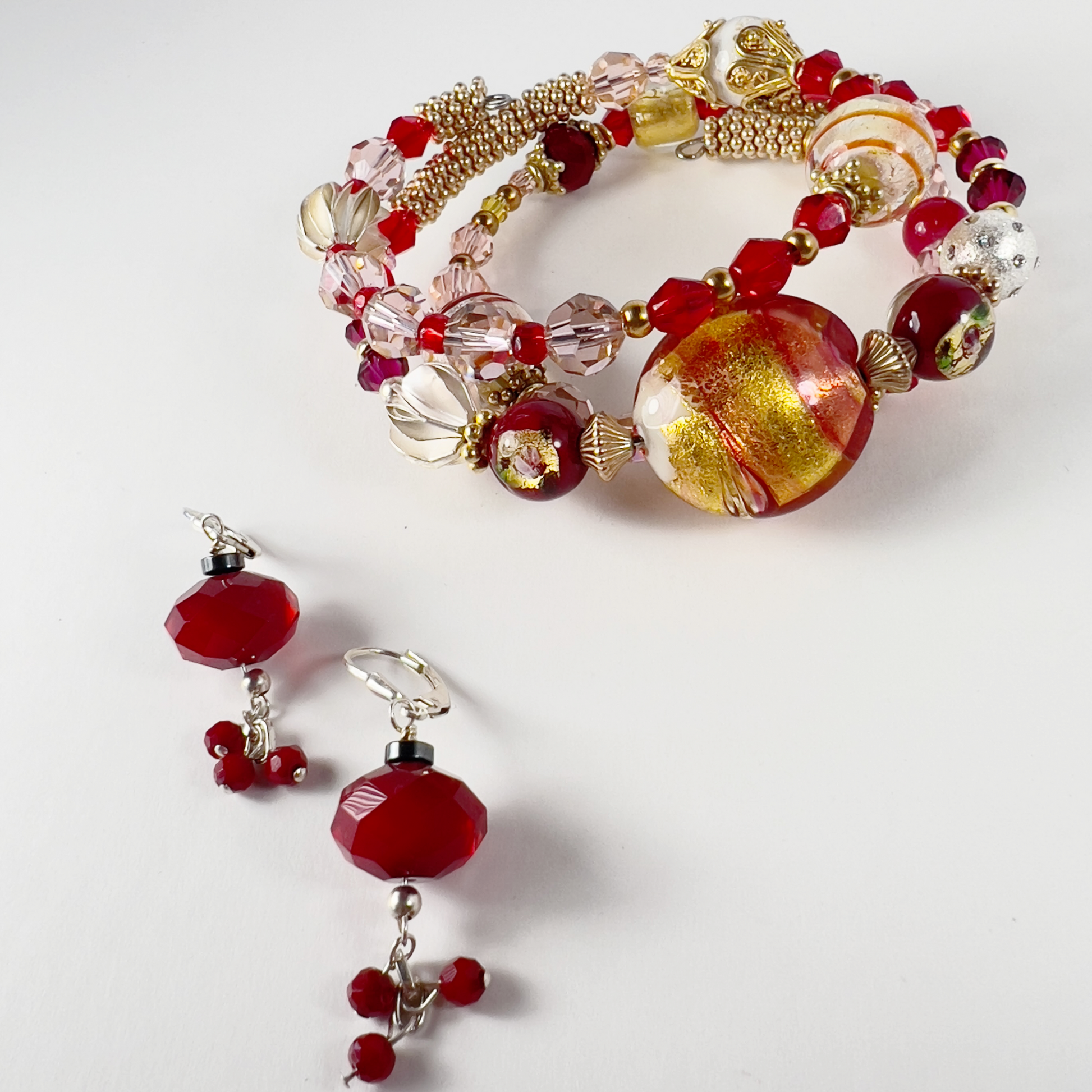 Delicate 3-wrap bracelet featuring a gold Italian Murano glass focal bead with swirls of orange, cream, red, and gold bead caps. Accented with sterling silver and gold-filled metals, handmade Hill Tribe sterling silver beads, and Swarovski crystals in pinks and reds.