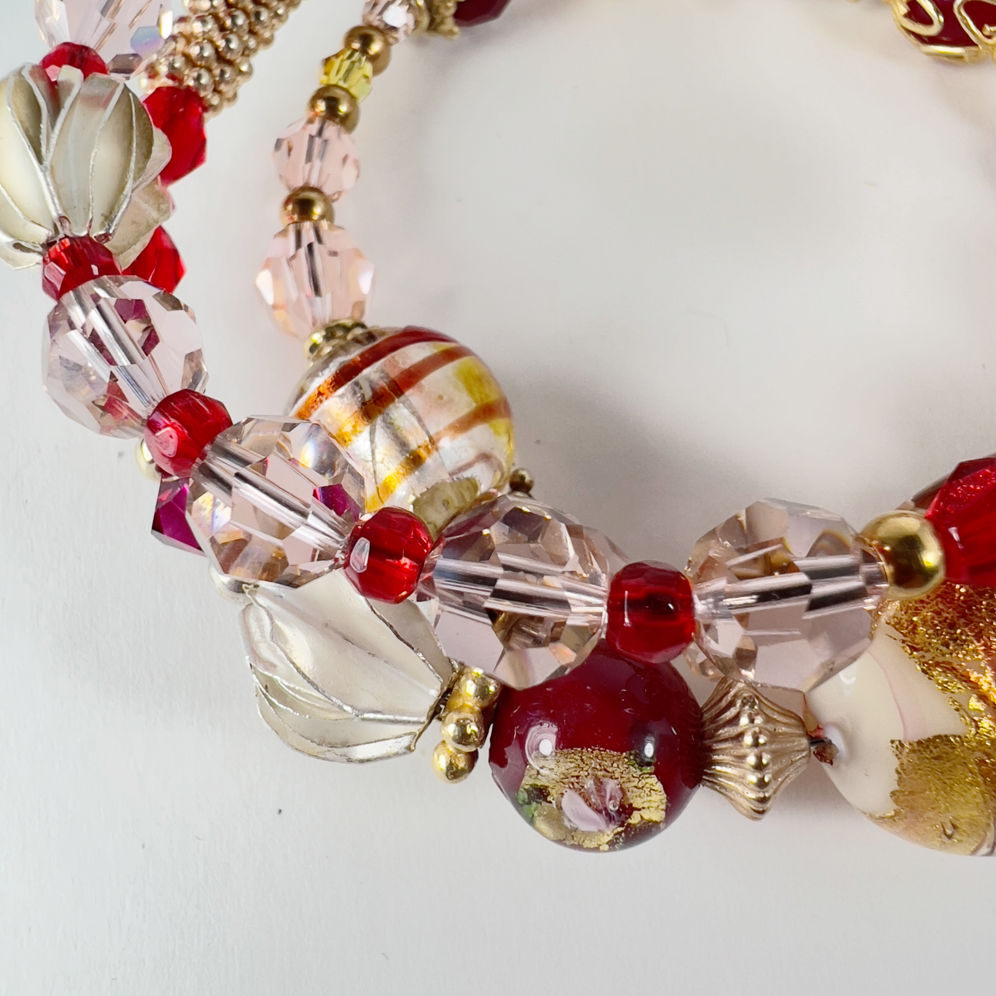 Delicate 3-wrap bracelet featuring a gold Italian Murano glass focal bead with swirls of orange, cream, red, and gold bead caps. Accented with sterling silver and gold-filled metals, handmade Hill Tribe sterling silver beads, and Swarovski crystals in pinks and reds.