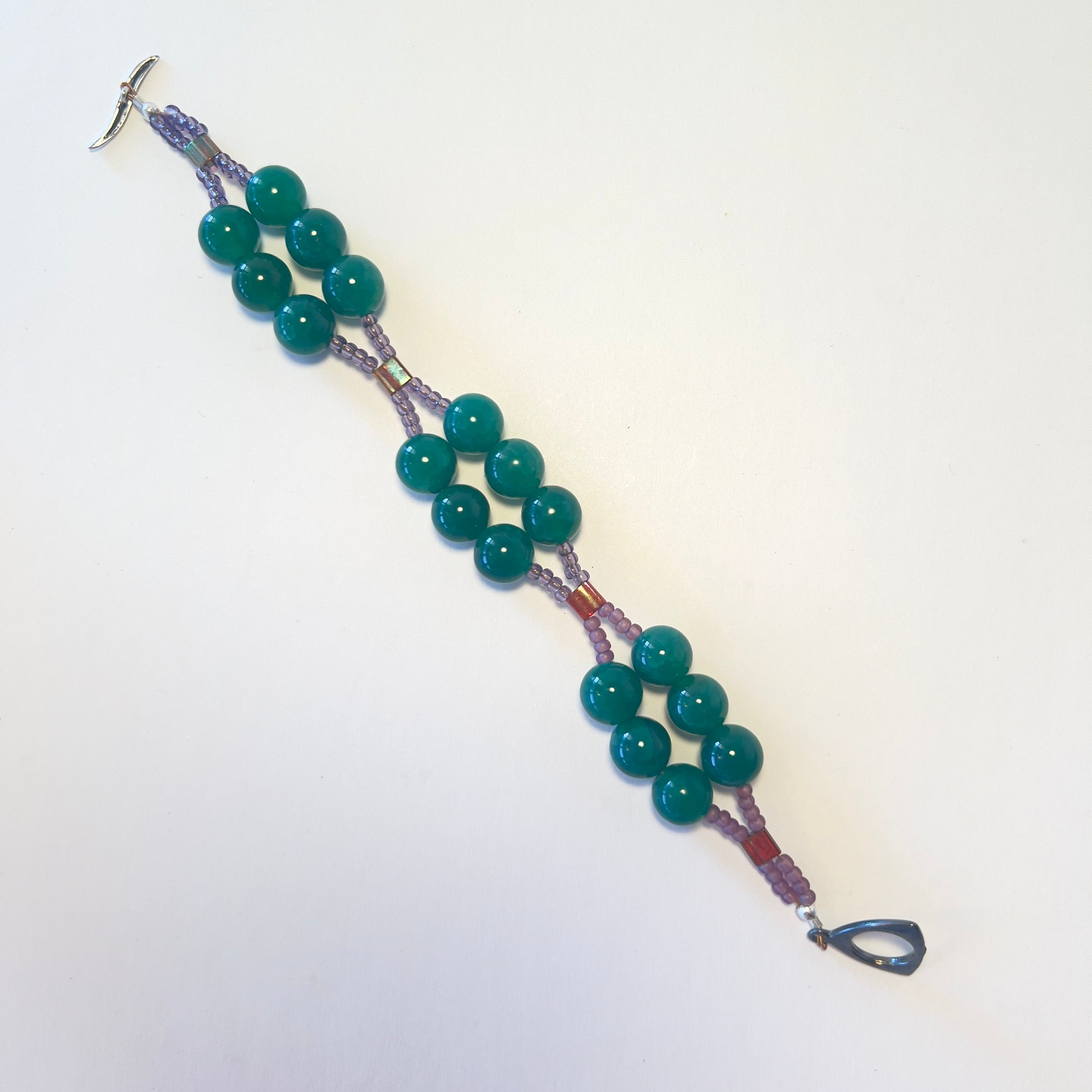 Charming double-strand bracelet featuring dark green quartz beads accented with purple seed beads, secured with a stylish toggle clasp