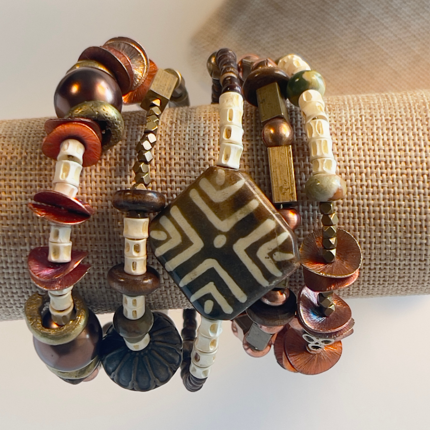 African style bracelet with hand-painted square ceramic bead, bold brass beads, cream bone spacers, square rectangle brass beads, copper round beads, and shiny textured copper flat spacers. Pair with a big copper medallion. Silver metal, one size fits all.