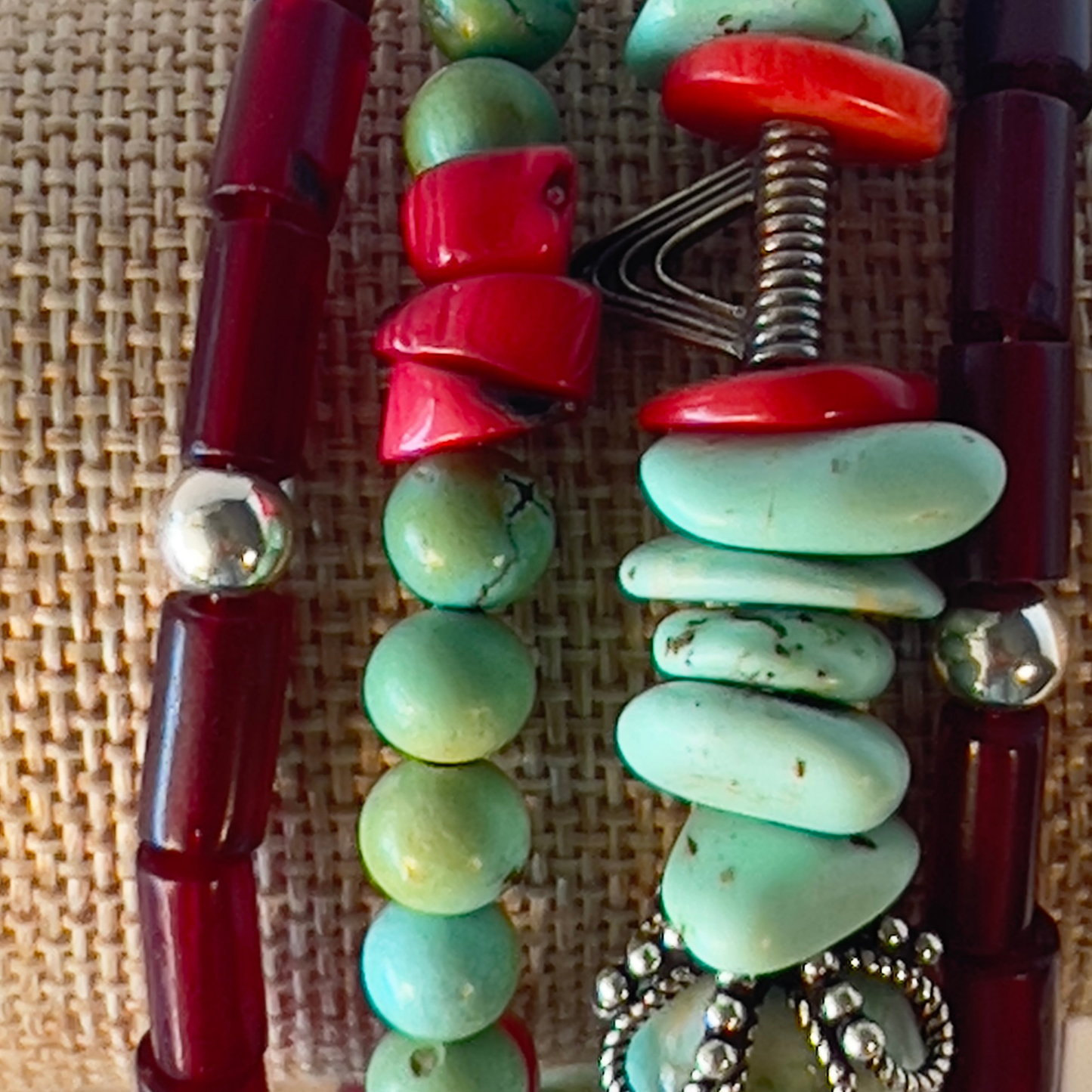 Natural turquoise polished beads with silver bead caps and textured round silver Bali beads. Red coral, round turquoise shapes, tubes of ruby beads, and sterling silver beads enhance the texture. Includes a marbled authentic turquoise nugget focal point. Silver metal, one size fits all.