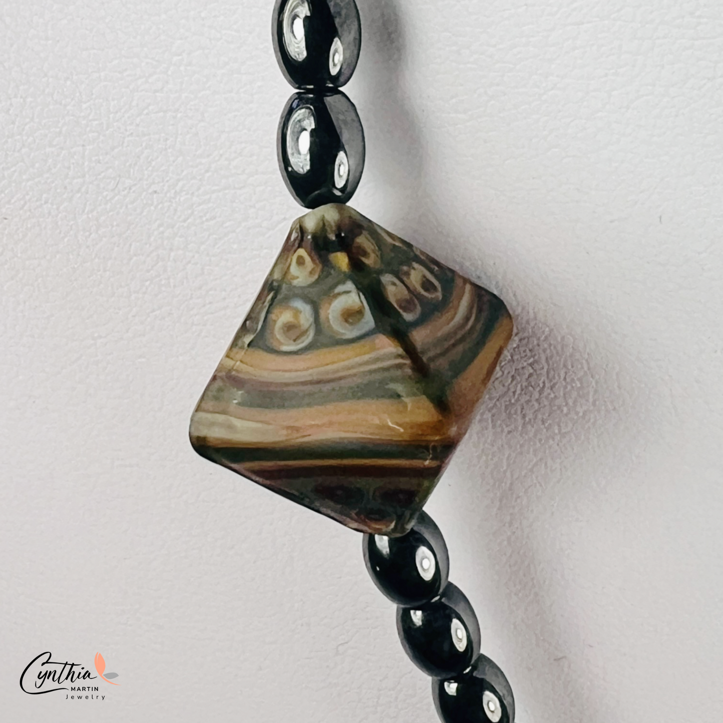 Necklace featuring an ancient two-eye Dzi bead from Nepal, paired with handcrafted pyramid-shaped ceramic beads and egg-shaped hematite beads, 15 inches with a 2-inch extender.
