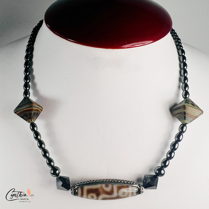 Necklace featuring an ancient two-eye Dzi bead from Nepal, paired with handcrafted pyramid-shaped ceramic beads and egg-shaped hematite beads, 15 inches with a 2-inch extender.
