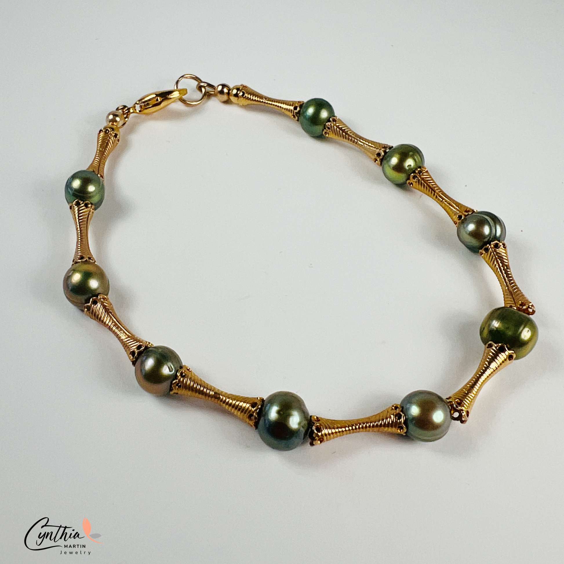 Stylish bracelet with iridescent green pearls and gold tube spacers, perfect for casual or corporate attire.
