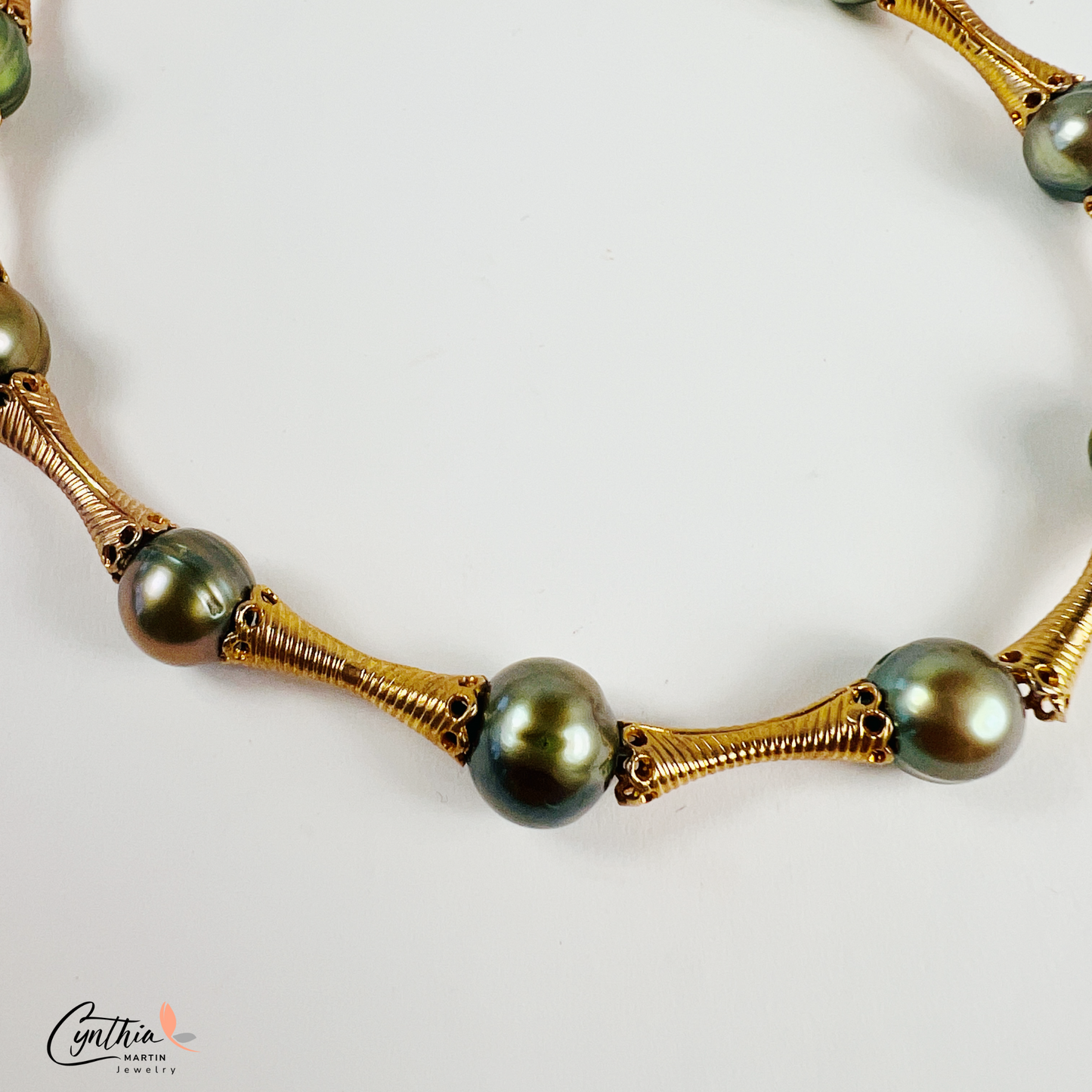 Stylish bracelet with iridescent green pearls and gold tube spacers, perfect for casual or corporate attire.
