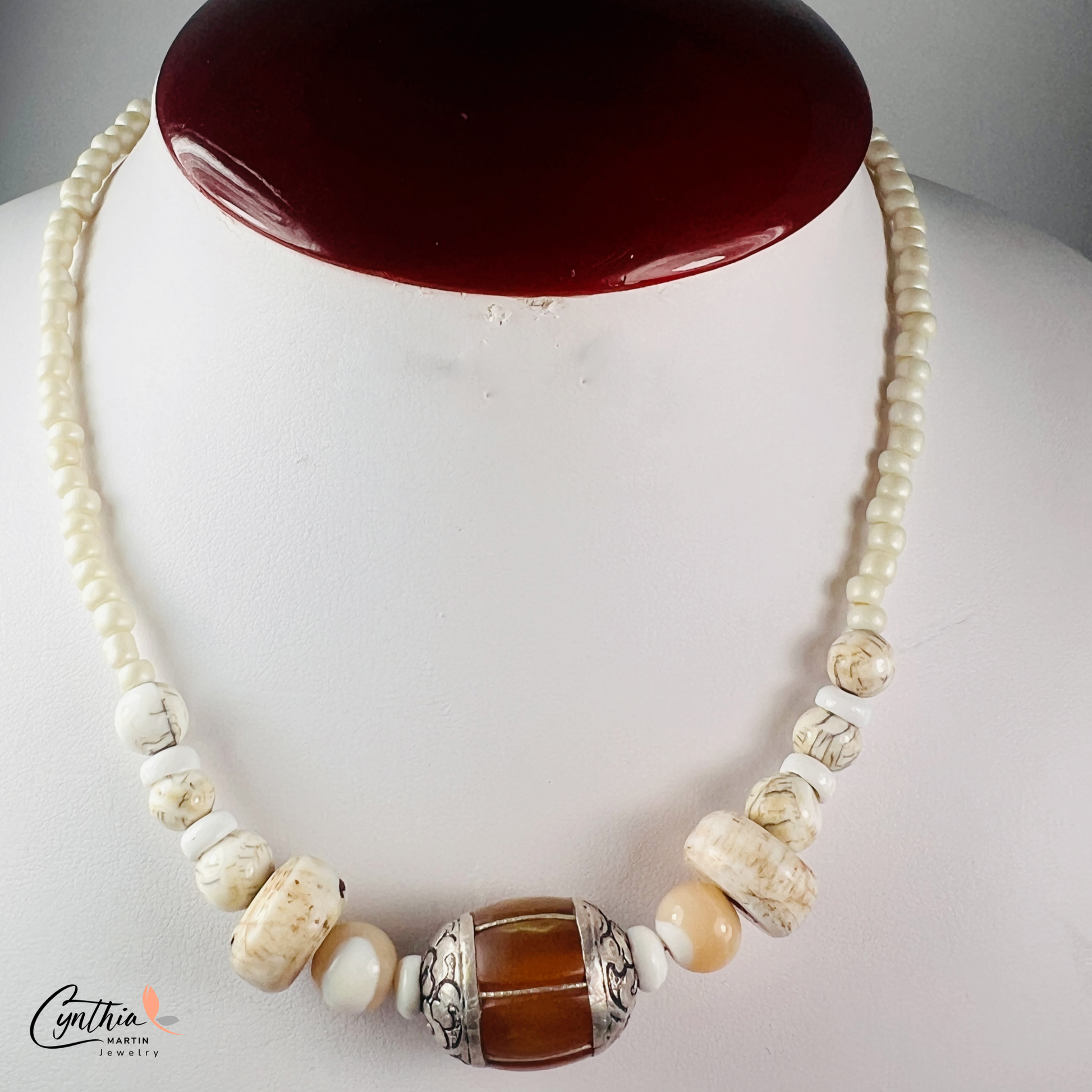 Necklace featuring an Indonesian silver and amber focal bead, accented with agate beads, natural stones, and glossy white beads, 15 inches with a 2-inch extender.
