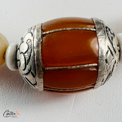 Necklace featuring an Indonesian silver and amber focal bead, accented with agate beads, natural stones, and glossy white beads, 15 inches with a 2-inch extender.
