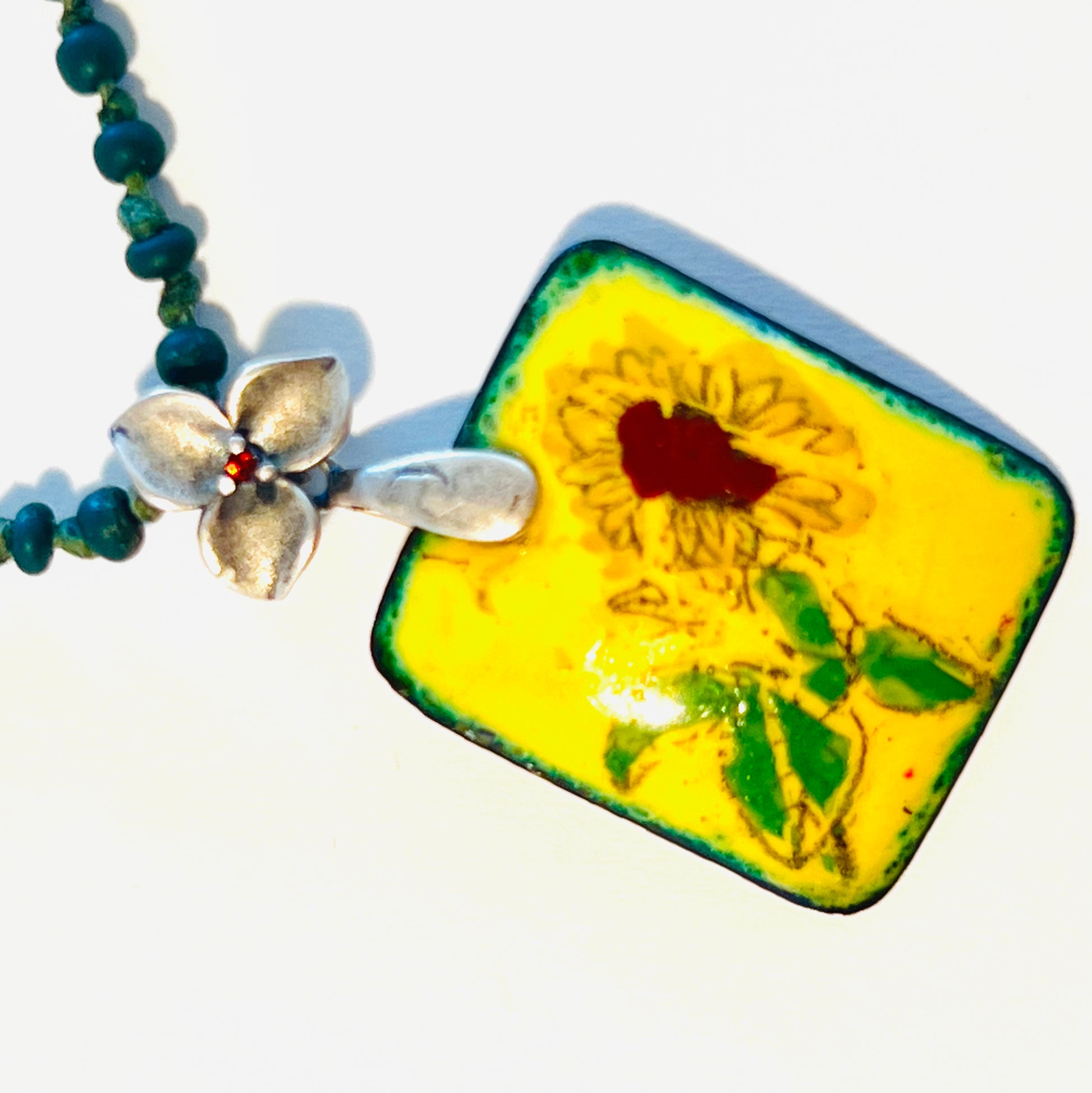 Charming necklace with vivid green beaded chain and enamel sunflower pendant. Bright green beads complement the vibrant yellow and brown sunflower for a cheerful, eye-catching look.