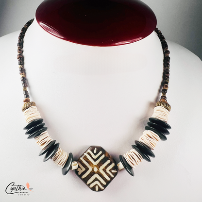 Hand-painted African tribal wooden focal bead necklace with black wooden discs, white paper beads, brown stones, and brass faceted beads, 15 inches with 2-inch extender.
