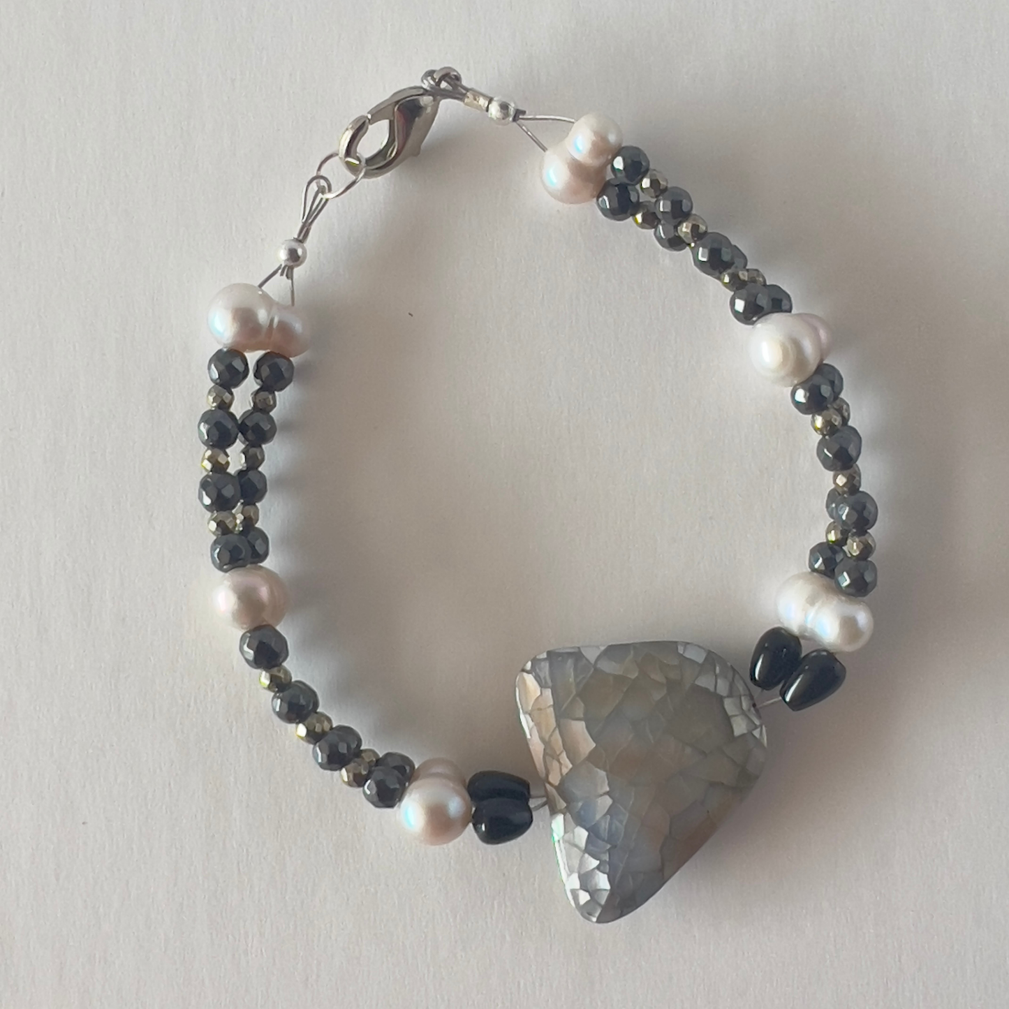 Double-strand gemstone bracelet of black lava rock beads with cultured pearls and mother-of-pearl focal bead, finished with a lobster clasp. Silver metal, wrist size 7 1/2 in.