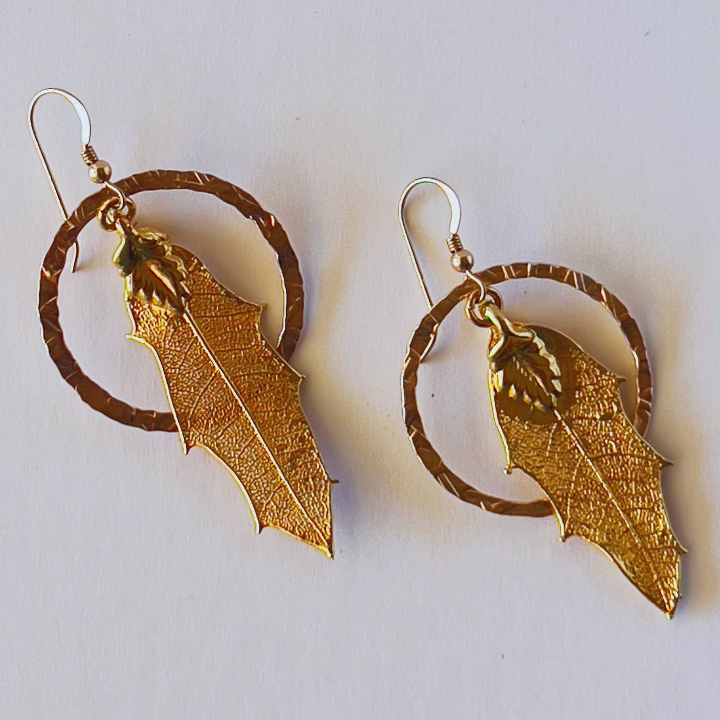 Hammered gold vermeil round loop earrings with a singular dangling leaf in the center.