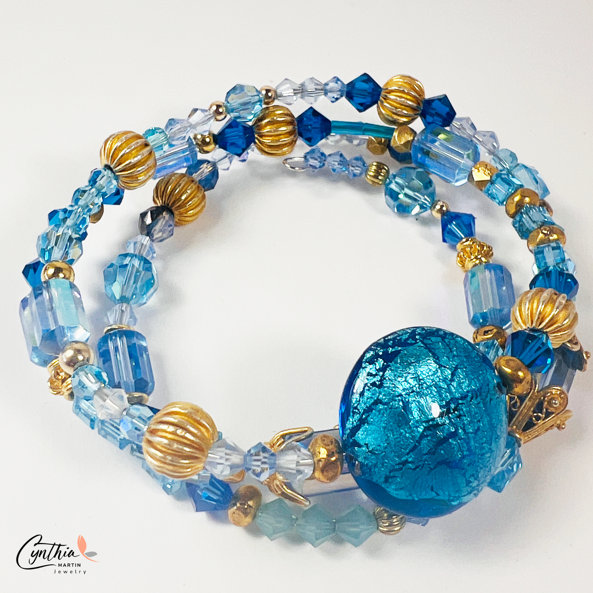 Three-wrap bracelet featuring a blue Italian Murano glass foiled focal bead, gold bead caps, transparent tube beads, and Swarovski crystals.
