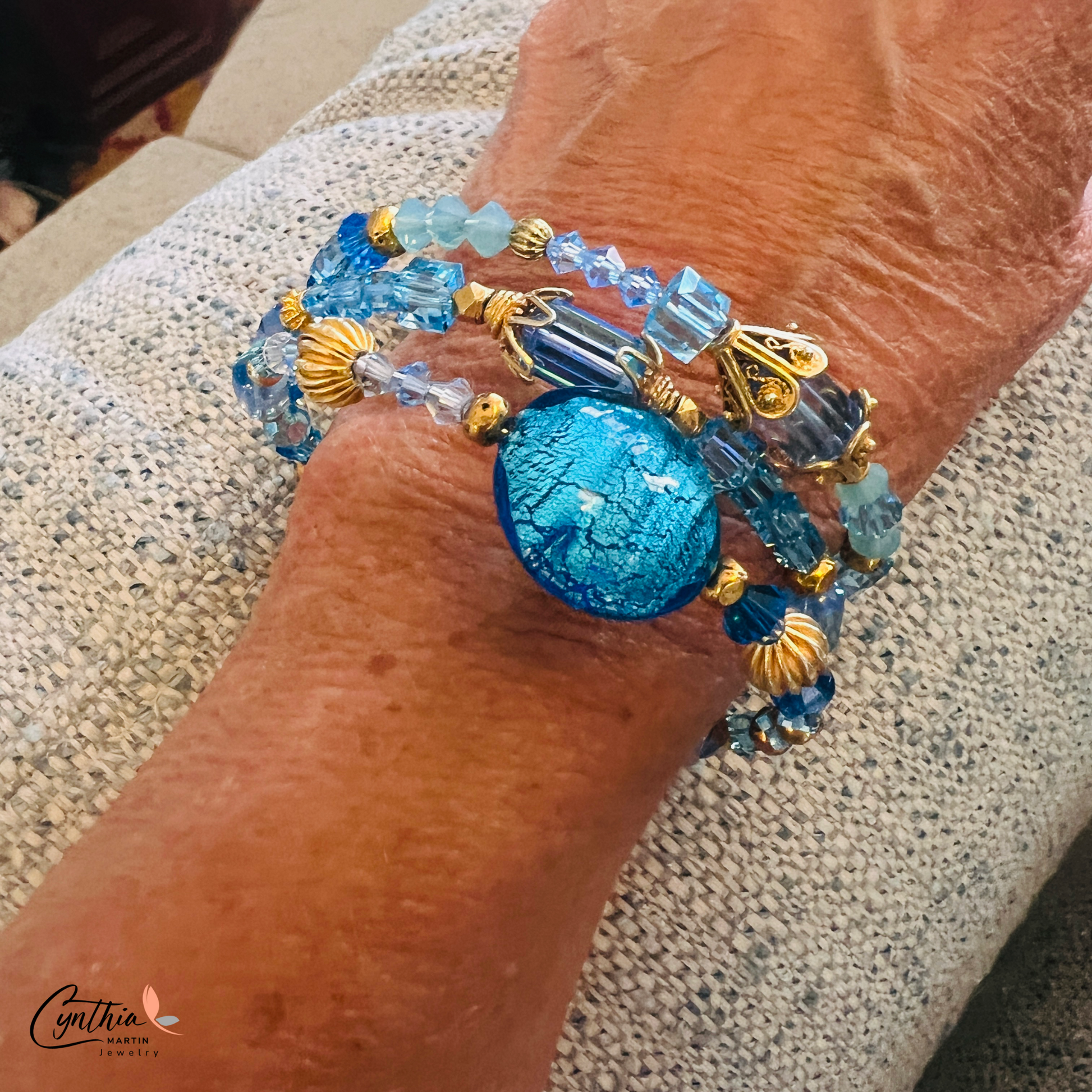 Three-wrap bracelet featuring a blue Italian Murano glass foiled focal bead, gold bead caps, transparent tube beads, and Swarovski crystals.
