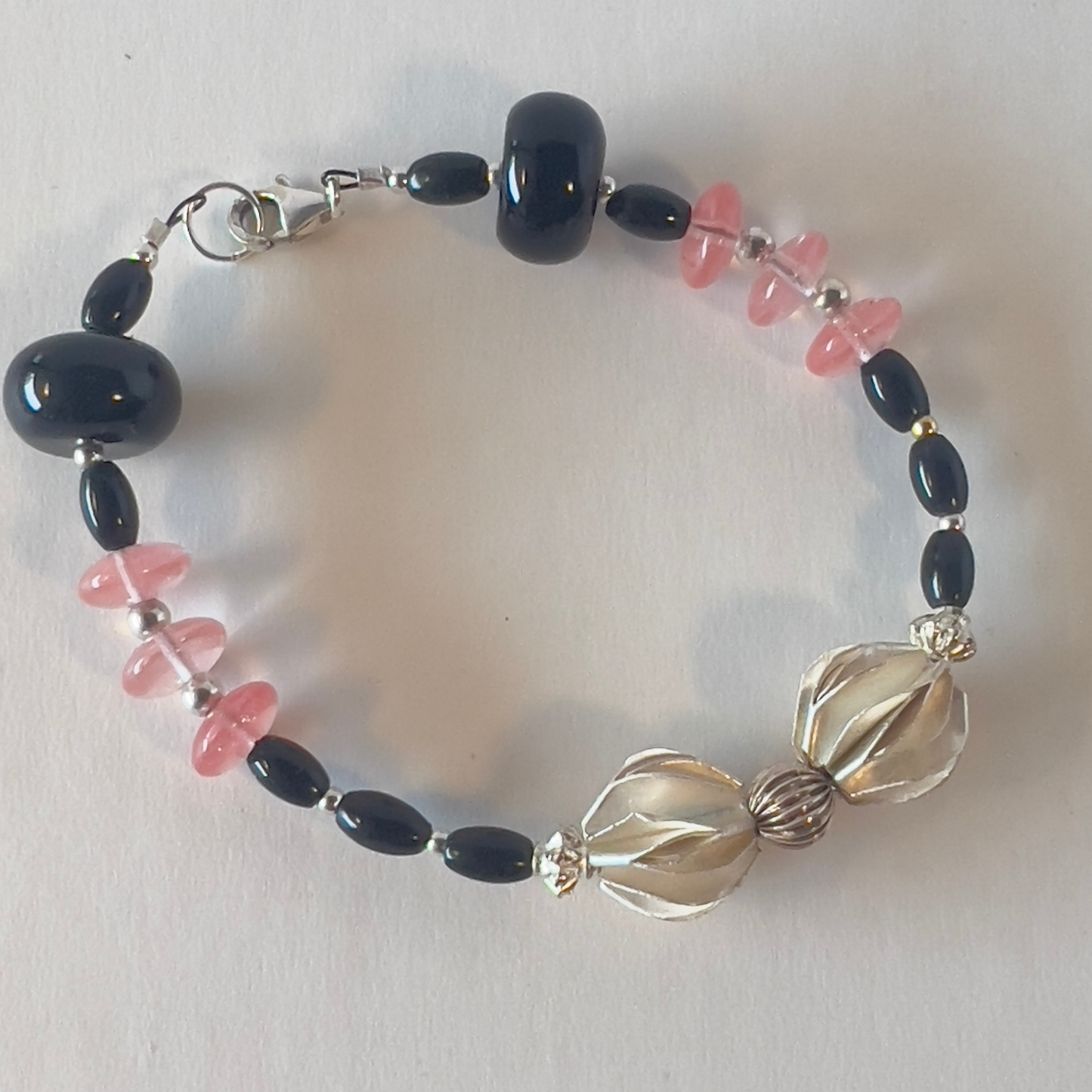 Nothing is as elegant as pink and black. Top it off with these stunning sterling silver beads designed by the Hilltribe Village in Thailand, where they pay wages and not slave labor. This is so balanced with the heavy beads on both sides. Silver metal, wrist size 6 3/4 in.