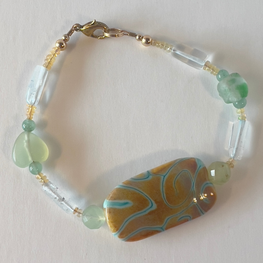 Transparency is the theme here. Quiet, sweet, with green sandstone beads, pale green heart-shaped beads, and beautiful ice green tube beads with splashes of honey-colored rondelles. The focal bead is designed by a dear friend, and I am so glad to be able to show it off to her. Gold metal, wrist size 7 1/2 in.