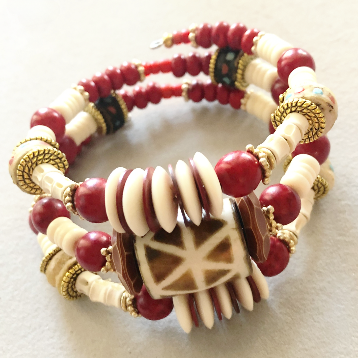 Three wrap bracelet with African-style hand-painted ceramic bead, bold red and gold spacers, cream bone spacers, and shiny textured copper flat spacers.