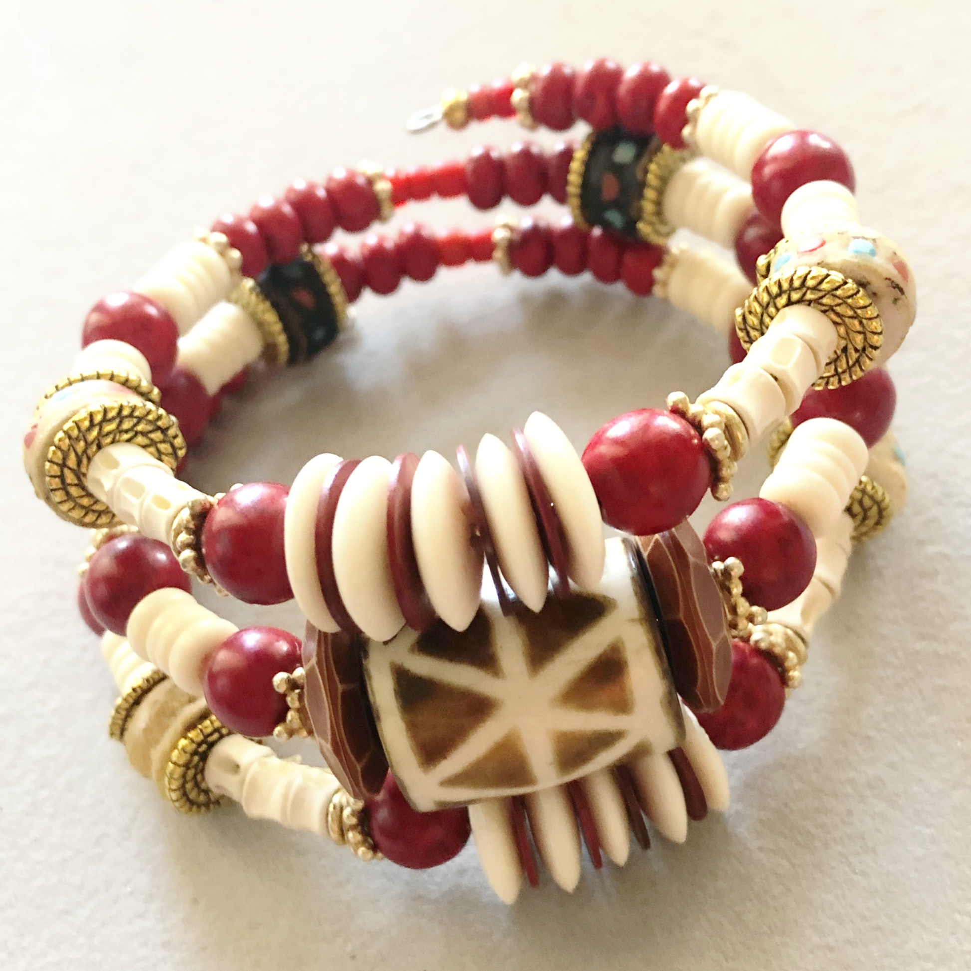 Three wrap bracelet with African-style hand-painted ceramic bead, bold red and gold spacers, cream bone spacers, and shiny textured copper flat spacers.